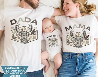 May include: Matching family shirts and baby bodysuit. The white shirts feature a deer graphic with the words "DADA" and "MAMA" above and "EST. 2025" below. The baby bodysuit says "THE BIG ONE".
