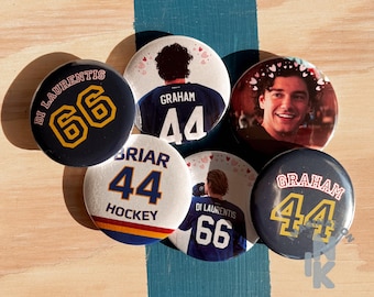 Peut inclure: Un ensemble de six badges ronds à épingle présentant des motifs sur le thème du hockey. Les badges affichent diverses images, dont une personne souriante, des joueurs en maillot avec les noms Di Laurentis, Graham et Briar, et les numéros 44 et 66.