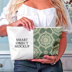 May include: A white and green patterned cosmetic bag with a gold zipper is held by a person. The bag has a white section with the text "SMART OBJECT MOCKUP" and a green section with a mandala design.