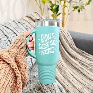 May include: A teal blue stainless steel tumbler with a lid and a straw. The tumbler has a handle and a white design that says "Your Design Here".