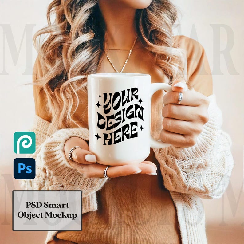May include: A white ceramic mug with a large handle, featuring the text "YOUR DESIGN HERE" in black. The mug is held by a person wearing a beige sweater. The image also includes the logos for Photoshop and Procreate, and the text "PSD Smart Object Mockup".