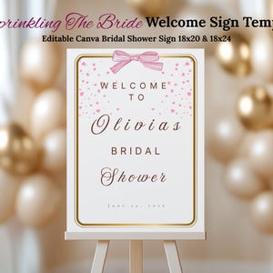 May include: A white welcome sign with gold trim and a pink bow at the top. The sign reads "Welcome to Olivias Bridal Shower" in elegant script. The sign is displayed on a white easel, with a blurred background of balloons.