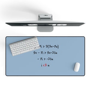May include: A blue desk mat with white keyboard and a white mouse. The mat has handwritten math equations on it: 7i > 3(3x-7u), 9x - 7i > 9x-21u, -7i > -21u, i < 3 u.