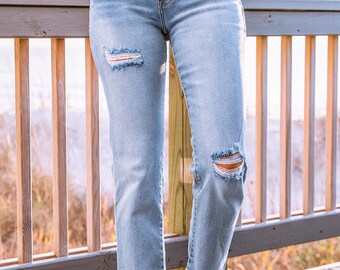 May include: A pair of light blue denim jeans with distressed details, featuring frayed hems and ripped knees. The jeans are shown on a wooden deck.