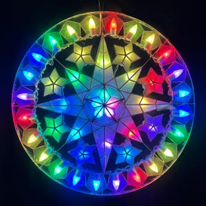 May include: A vibrant, illuminated star-shaped Christmas decoration. The design features a central star with multiple points, surrounded by a ring of colorful lights. The lights are arranged in a rainbow pattern, creating a festive and eye-catching display.