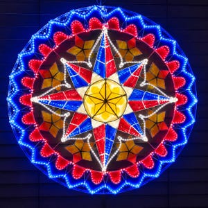 May include: A circular decorative lantern featuring a central yellow star surrounded by alternating red and blue star-shaped panels. The outer edge is scalloped with bright blue LED lights, while white LED lights outline the inner star patterns.