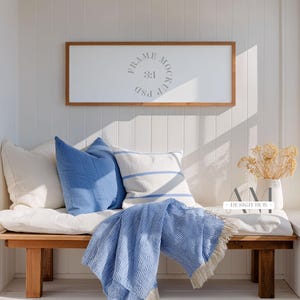 May include: A wooden bench with white and blue pillows, a blue striped blanket, and a framed sign that reads "FRAME MOCKUP 3:1 PSD". A white vase with dried flowers sits on the bench.