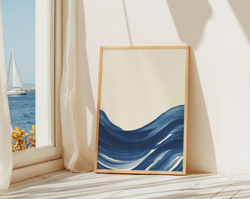 May include: A framed abstract painting of blue waves on a cream background. The painting is in a light wood frame and is leaning against a white wall.
