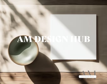 May include: A white card with the text "AM DESIGN HUB" on a beige surface with a green ceramic bowl and shadows from sunlight.
