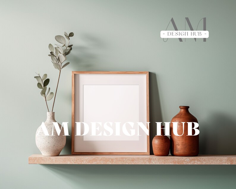 May include: A wooden frame with a white mat and a white background sits on a shelf with a white vase with green leaves, a small brown ceramic vase, and a larger brown ceramic vase. The text "AM DESIGN HUB" is printed in white on the shelf.