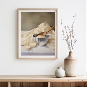 May include: A framed still life painting of a white bowl filled with flour, a wooden spoon, and a white cloth on a light gray surface.