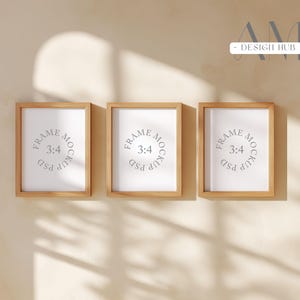 May include: Three wooden picture frames with white inserts are mounted on a beige wall. Each frame has a rectangular shape with a light brown finish. The inserts feature the text "FRAME MOCKUP 3:4" in a circular design.
