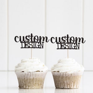 Pode incluir: Dois cupcakes brancos com cobertura branca, cobertos com toppers de cupcake pretos que dizem "custom design".