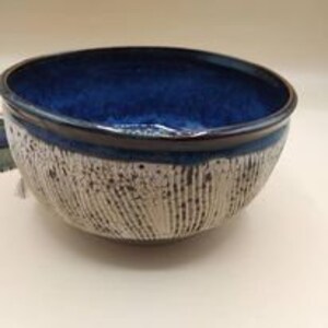 Peut inclure: Un grand bol en céramique blanche avec un glaçage bleu et un extérieur texturé et côtelé. Le bol a un bord brun foncé.