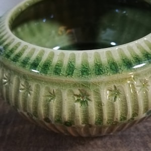 Peut inclure: Un pot en céramique vert avec un glaçage texturé craquelé et un motif de étoiles en relief. Le pot a une large ouverture ronde et un fond légèrement arrondi.