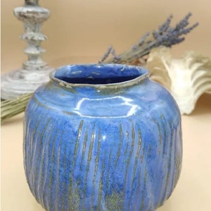 Peut inclure: Un vase rond en céramique bleu avec des lignes verticales texturées. Le vase a une large ouverture et une finition brillante. De la lavande séchée et un coquillage décoratif sont en arrière-plan. Un élément de décoration pour la maison.