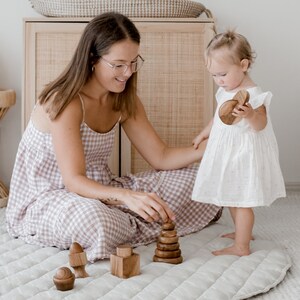 May include: A set of natural wooden stacking toys including a tiered cone, a cube with a cylindrical top, and a small rounded piece with a base. The smooth, polished brown wood pieces are arranged on a quilted surface for tactile play and exploration.