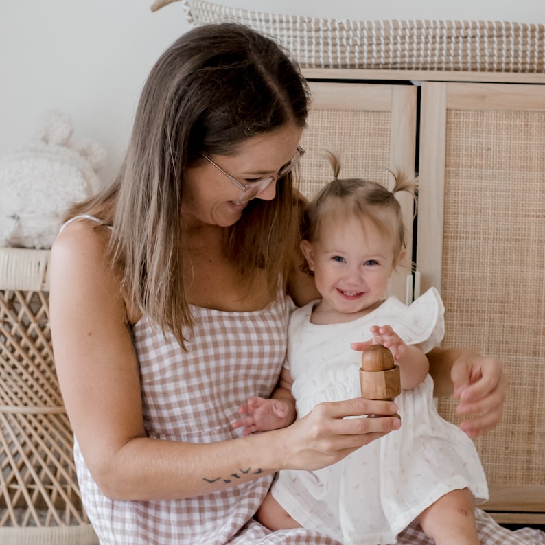May include: A small, smooth, cylindrical wooden toy with a rounded top piece that fits into a base. The object is held in hands, showcasing its natural light brown wood grain, simple geometric shape, and polished finish, designed for tactile play.