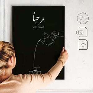 May include: Black and white line art print of a hand pouring tea from a teapot into three cups. The Arabic word "مرحبا" is written above the image, which translates to "Welcome".