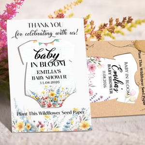 May include: Baby shower favor cards with a baby onesie cutout design. The white card features text that reads "Thank you for celebrating with us! Baby in Bloom, Emilia's Baby Shower 11.08.2026." The card is decorated with floral illustrations.