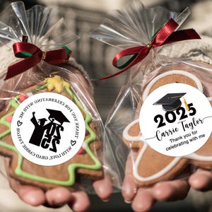 May include: Two gingerbread cookies decorated with graduation themed stickers. One cookie is shaped like a Christmas tree and the other is shaped like a gingerbread man. The stickers feature a graduation cap, the year 2025, and the text "Carrie Taylor Thank you for celebrating with me".
