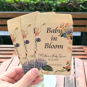 Pode incluir: Três envelopes de papel castanho com desenhos florais e o texto "Baby in Bloom" e "Madison's Baby Shower 05.26.2025 Wildflower Seeds".