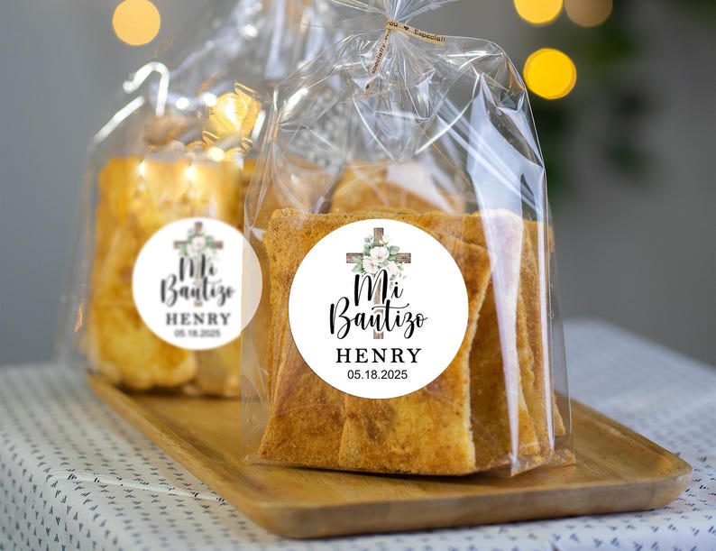 May include: A clear plastic bag filled with small, rectangular pieces of bread. The bag has a white sticker with a cross and flowers, and the text "Mi Bautizo HENRY 05.18.2025".