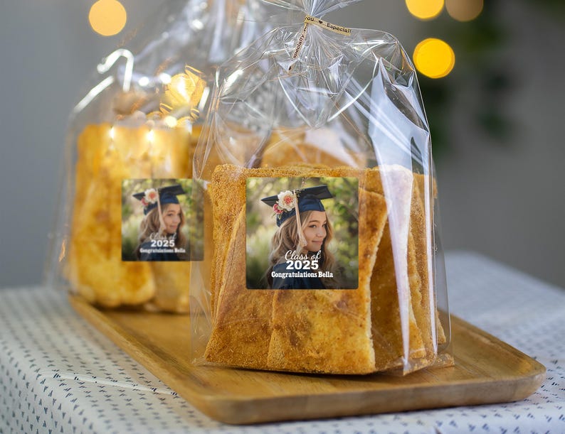 K&ouml;nnte beinhalten: Eine durchsichtige Plastikt&uuml;te gef&uuml;llt mit knusprigen, goldbraunen Crackern. Die T&uuml;te hat ein personalisiertes Etikett mit einem Foto eines Absolventen, der eine Kappe und eine Robe tr&auml;gt, und dem Text "Klasse von 2025 Herzlichen Gl&uuml;ckwunsch Bella".