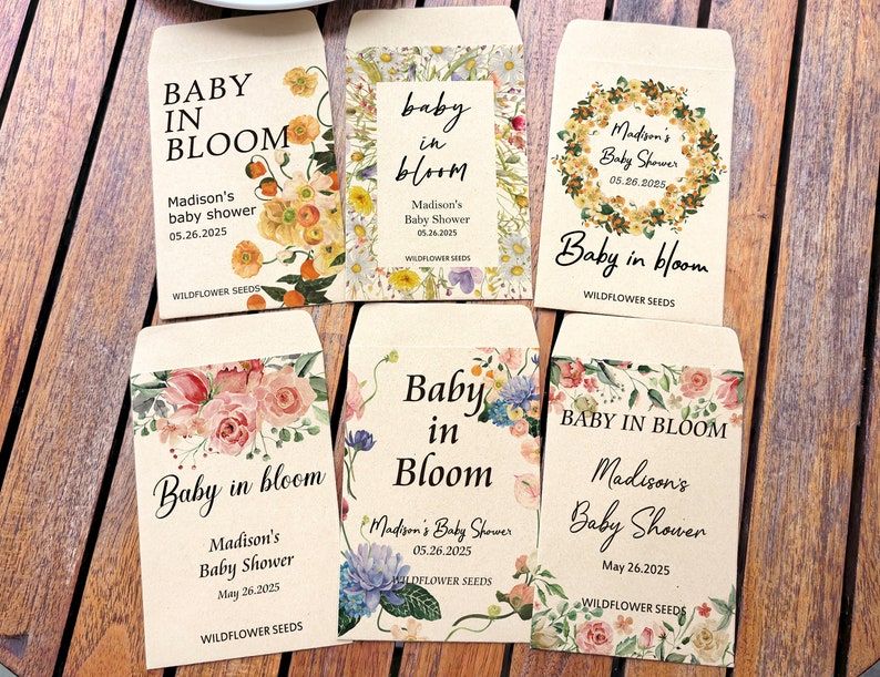 May include: A collection of seed packets with floral designs and the text "Baby in Bloom." Each packet is personalized for Madison's baby shower, with the date May 26, 2025, and the words "Wildflower Seeds."