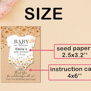 May include: A baby shower announcement card with a floral design. The card features the text "Baby in Bloom" and the baby's name, Emilia, with the date 11.08.2026. The seed paper measures 2.5x3.2 inches, and the instruction card is 4x6 inches.
