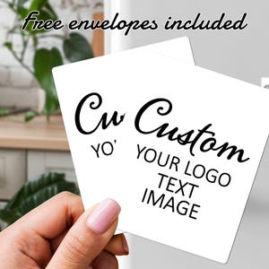 Pode incluir: Dois cartões quadrados brancos com as palavras "Cu Custom" e "YO' YOUR LOGO TEXT IMAGE" em escrita preta. As palavras "Free envelopes included" estão escritas em itálico no topo. Os cartões são segurados em uma mão.
