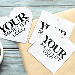 Puede incluir: Etiquetas blancas en forma de corazón y cuadradas con el texto "YOUR IMAGE / TEXT LOGO" en negro. Las etiquetas están sobre una superficie marrón claro, con un cuenco de hierbas secas y un fondo de madera azul claro.