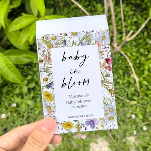 May include: A white seed packet with a floral design and the words "baby in bloom." The packet includes the text "Madison's Baby Shower 05.26.2025" and "WILDFLOWER SEEDS."