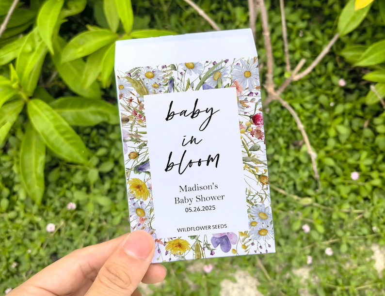 May include: A white seed packet with a floral design and the words "baby in bloom." The packet includes the text "Madison's Baby Shower 05.26.2025" and "WILDFLOWER SEEDS."