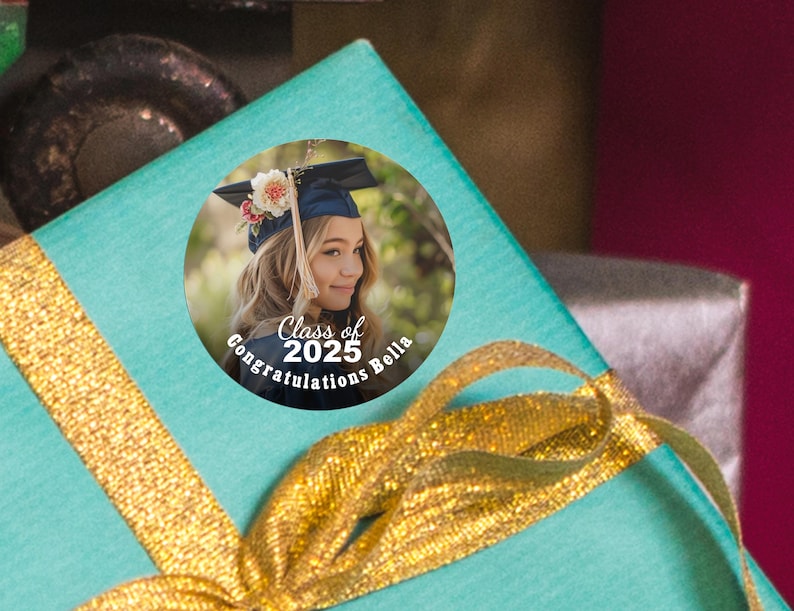 K&ouml;nnte beinhalten: Ein runder Abschlussaufkleber mit einem Foto einer jungen Frau in einer Abschlusscap und -robe. Der Aufkleber tr&auml;gt den Text "Class of 2025" und "Congratulations Bella".