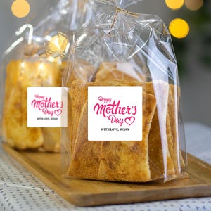 May include: A clear plastic bag filled with crispy, golden brown breadsticks. The bag has a white label with the text "Happy Mother's Day" in pink cursive lettering and the words "With love, Susan" in black text.