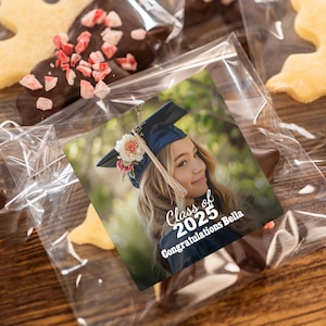 K&ouml;nnte beinhalten: Ein Abschlussgeschenk mit einem personalisierten Foto einer jungen Frau, die eine Abschlusscap und eine Robe tr&auml;gt. Das Geschenk beinhaltet einen Schokoladen-&uuml;berzogenen Keks mit einem Aufkleber, auf dem "Klasse von 2025 Herzlichen Gl&uuml;ckwunsch Bella" steht.