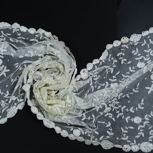May include: A white lace shawl with a delicate floral pattern and a scalloped edge.