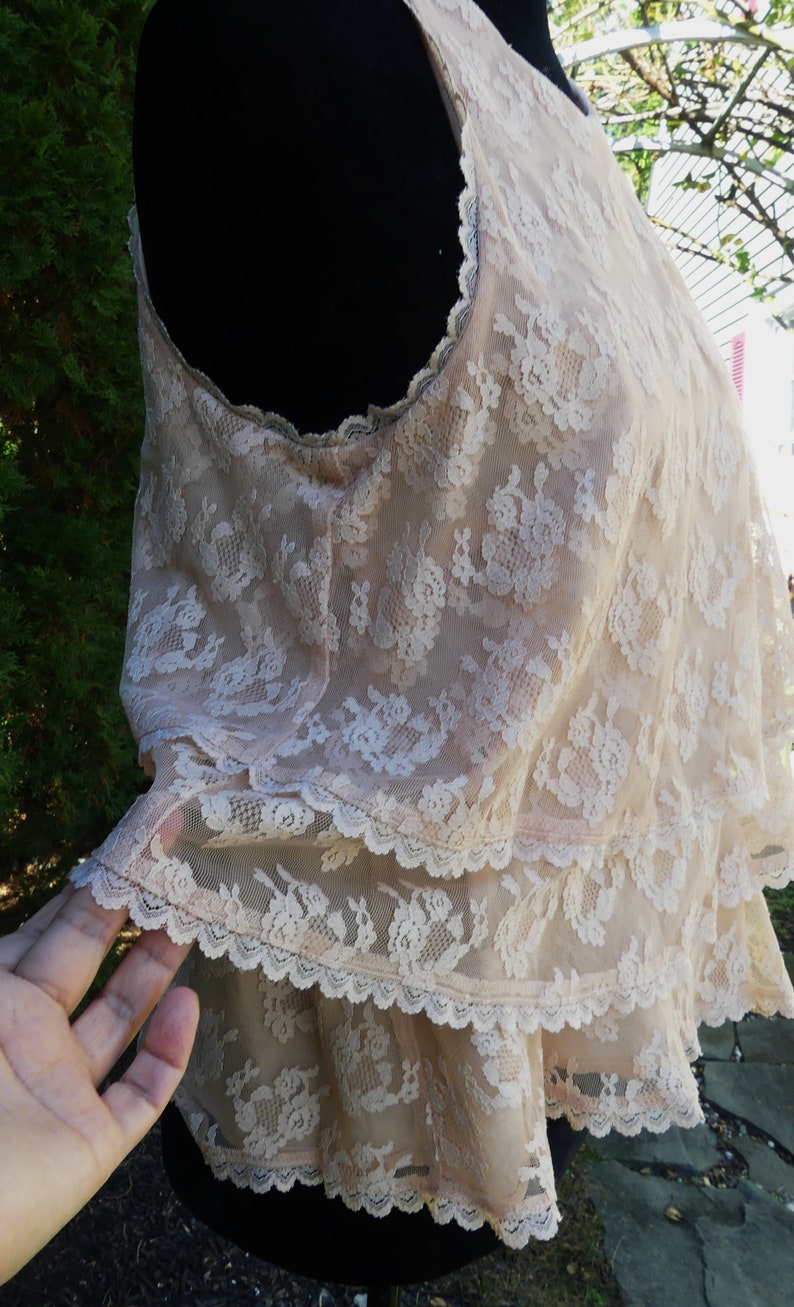 K&ouml;nnte beinhalten: Ein zartes, hellrosa Spitzenoberteil mit einem mehrlagigen R&uuml;schen-Design. Das Oberteil ist &auml;rmellos und hat einen runden Ausschnitt.