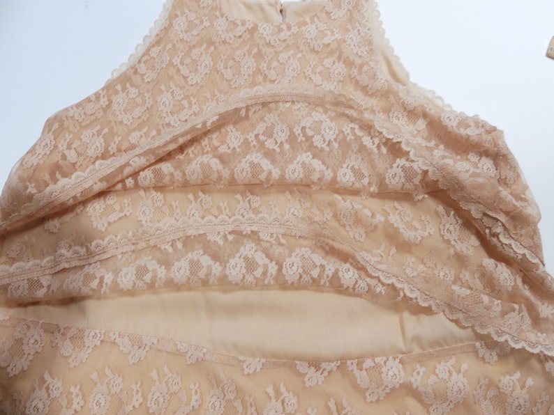 K&ouml;nnte beinhalten: Ein beigefarbenes, &auml;rmelloses Oberteil aus Spitze mit einem mehrschichtigen Design. Das Oberteil besteht aus zarter Spitze mit einem Blumenmuster.