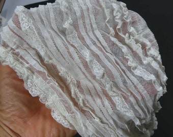 Puede incluir: Tela de encaje blanca con un borde rizado. El encaje tiene un patrón delicado y es suave y transparente.