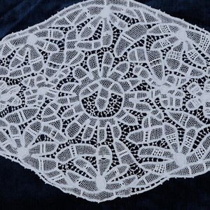 May include: White lace doily with a delicate, intricate pattern. The doily is circular and has a scalloped edge.
