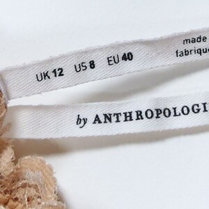 K&ouml;nnte beinhalten: Wei&szlig;es Etikett mit schwarzem Text "UK 12 US 8 EU 40" und "by ANTHROPOLOGIE"  Hergestellt in Vietnam