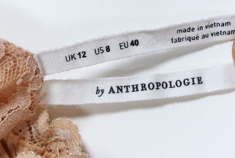 K&ouml;nnte beinhalten: Wei&szlig;es Etikett mit schwarzem Text "UK 12 US 8 EU 40" und "by ANTHROPOLOGIE"  Hergestellt in Vietnam