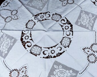 Könnte beinhalten: Weiße Baumwolltischdecke mit aufwendiger Spitzenbordüre. Das Design zeigt ein großes kreisförmiges Motiv in der Mitte, umgeben von kleineren Blumenmustern.