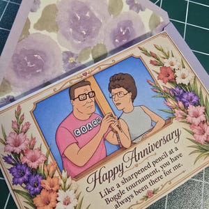 May include: An anniversary card featuring a cartoon couple with the text "Happy Anniversary." The card includes a floral arrangement of pink, purple, and white gladiolus. The envelope has a floral pattern.