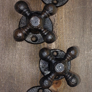 May include: Four black cast iron faucet knobs with a rustic finish. The knobs are mounted on a wooden surface.