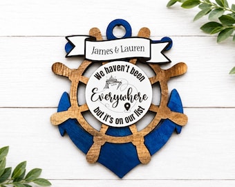 May include: Wooden nautical-themed wall decoration shaped like an anchor. The anchor is blue and brown, with a ship's wheel in the centre. A banner at the top reads "James & Lauren." The centre circle says "We haven't been Everywhere but it's on our list."