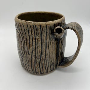 May include: A ceramic mug with a wood grain design. The mug has a brown glaze with black lines and a handle.