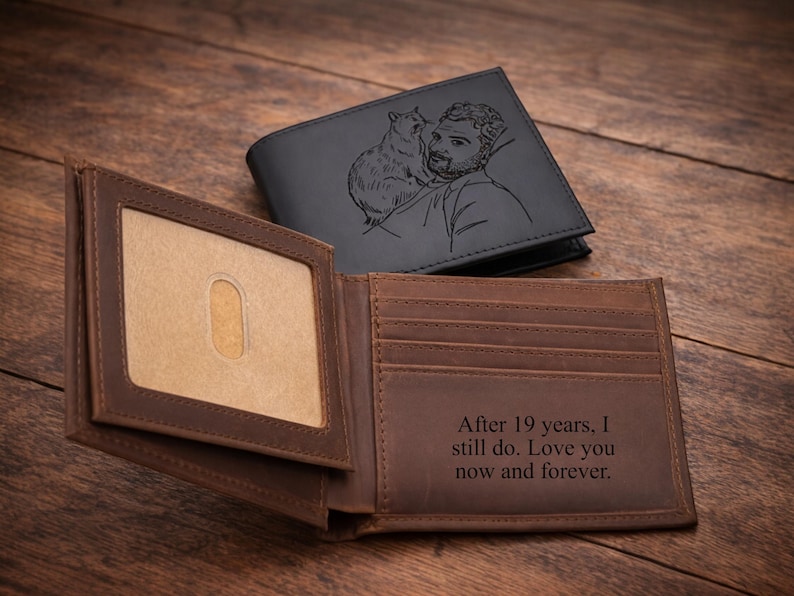 May include: Two leather wallets, one open and one closed, on a wooden surface. The open wallet is brown with a clear ID window and text that reads, "After 19 years, I still do. Love you now and forever." The closed wallet is black with an engraved image.